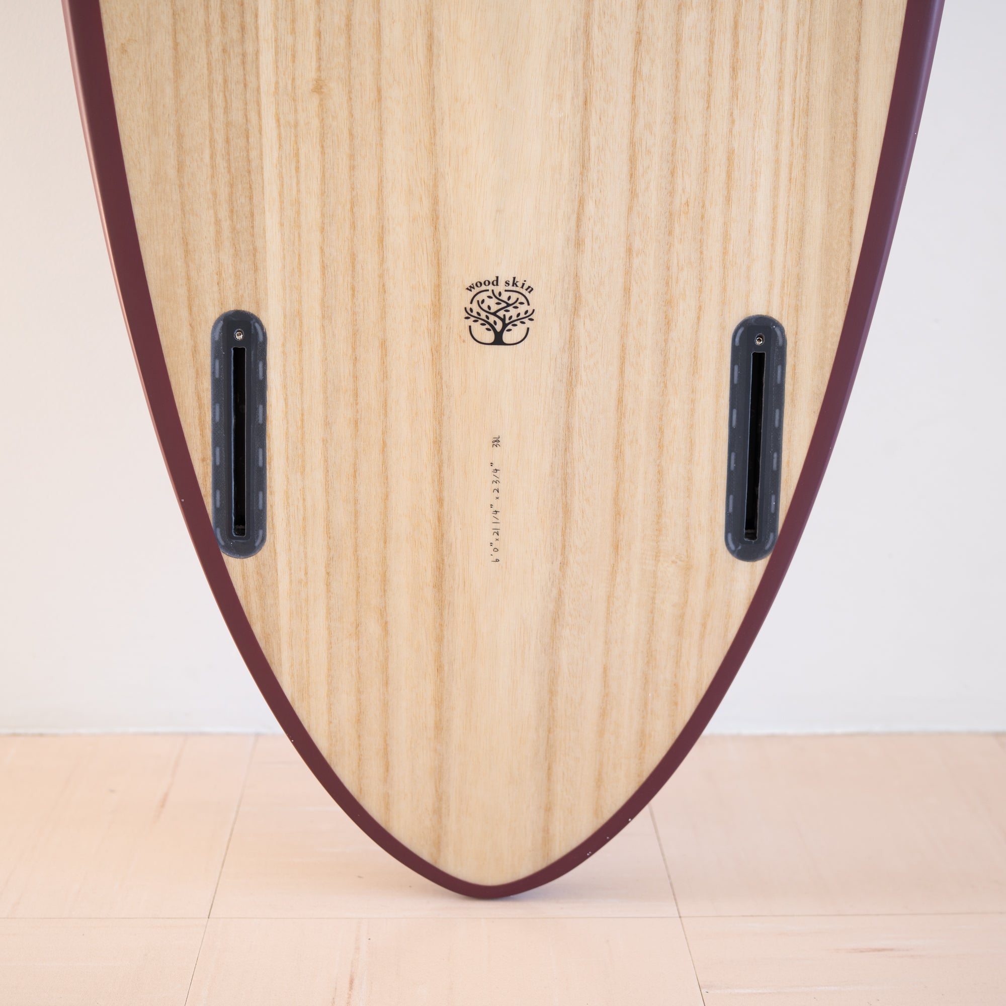 木製のサーフボードの底部に「wood skin」と書かれたロゴと穴が見える